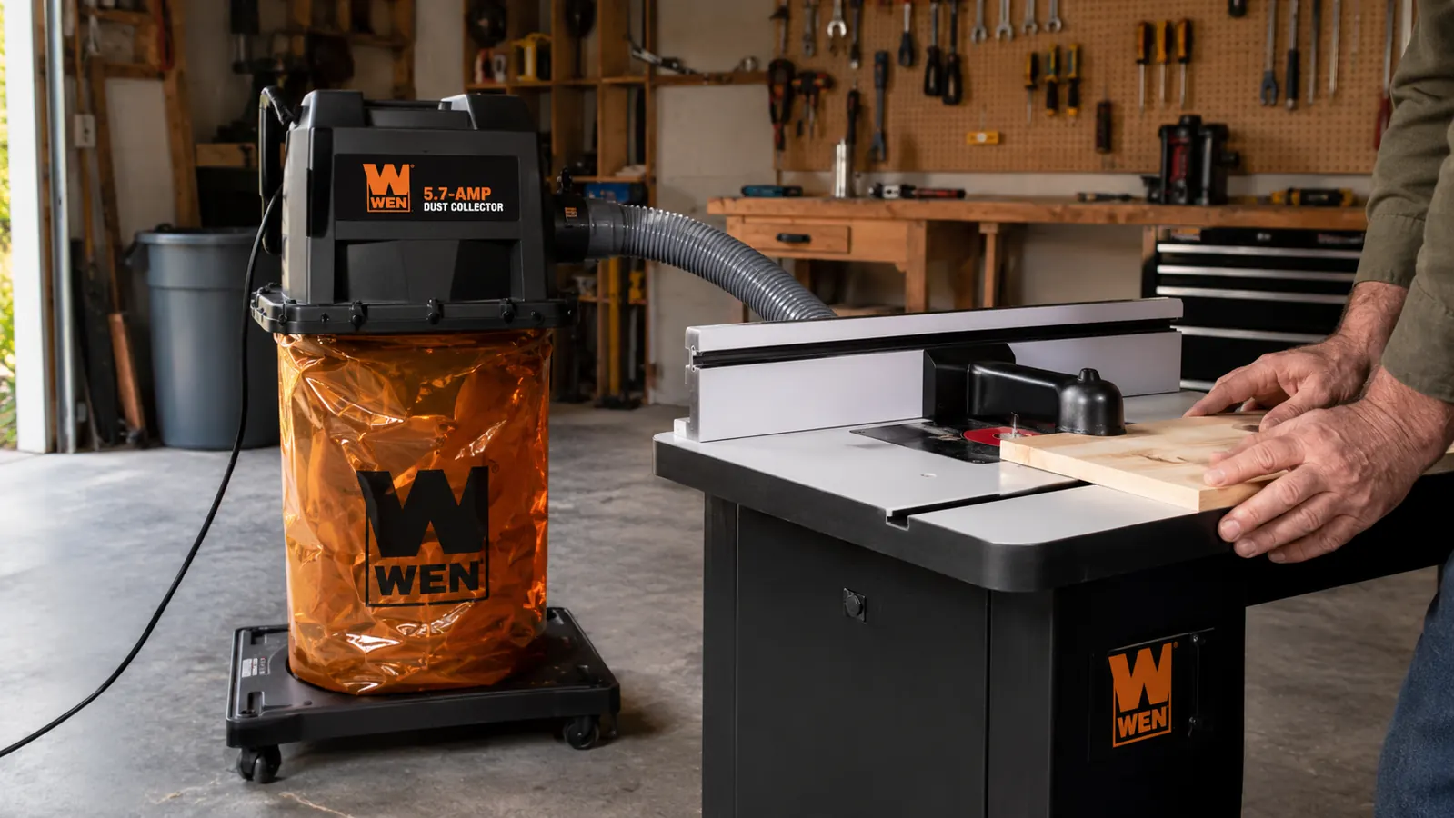 WEN dust collector with 12-gallon bag sitting on its mobile base next to a workbench, 4-inch hose running to a router table