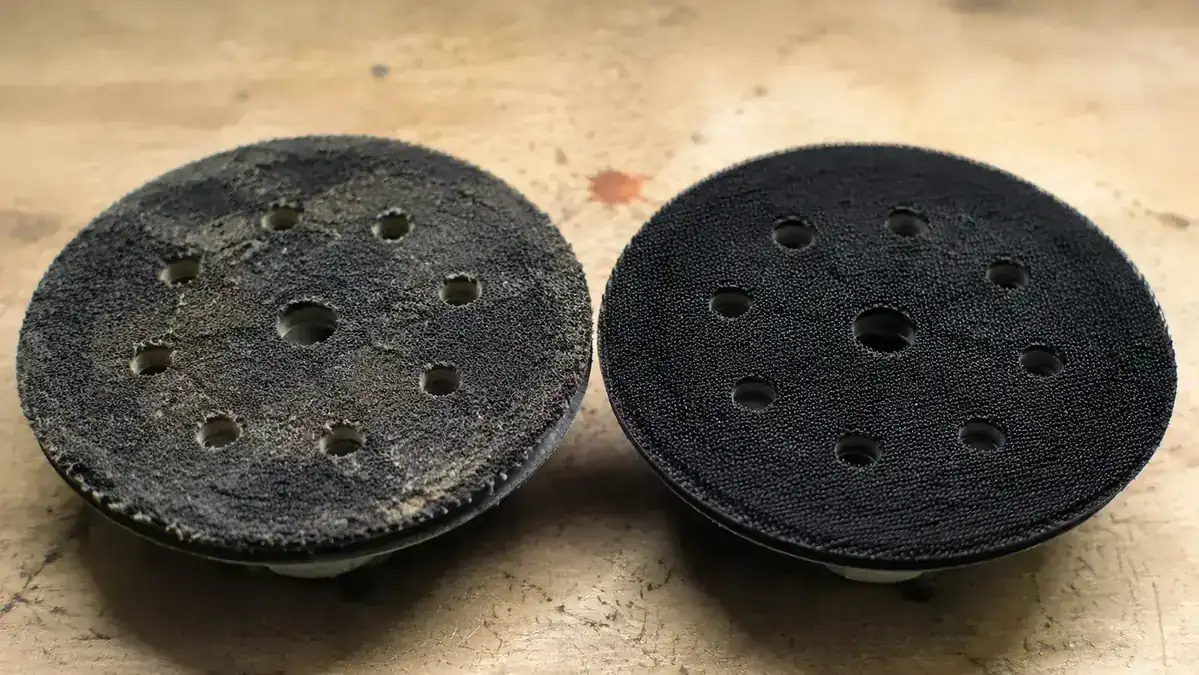 Close-up comparison of a worn hook-and-loop sanding pad versus a new pad showing backing deterioration