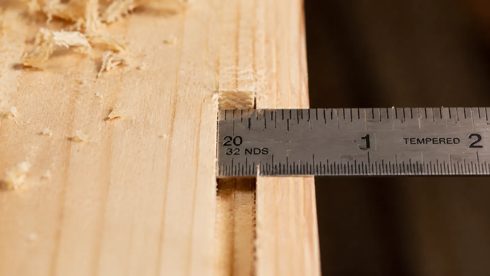 Test dado cut in scrap pine with a ruler checking the width fits a plywood shelf snugly