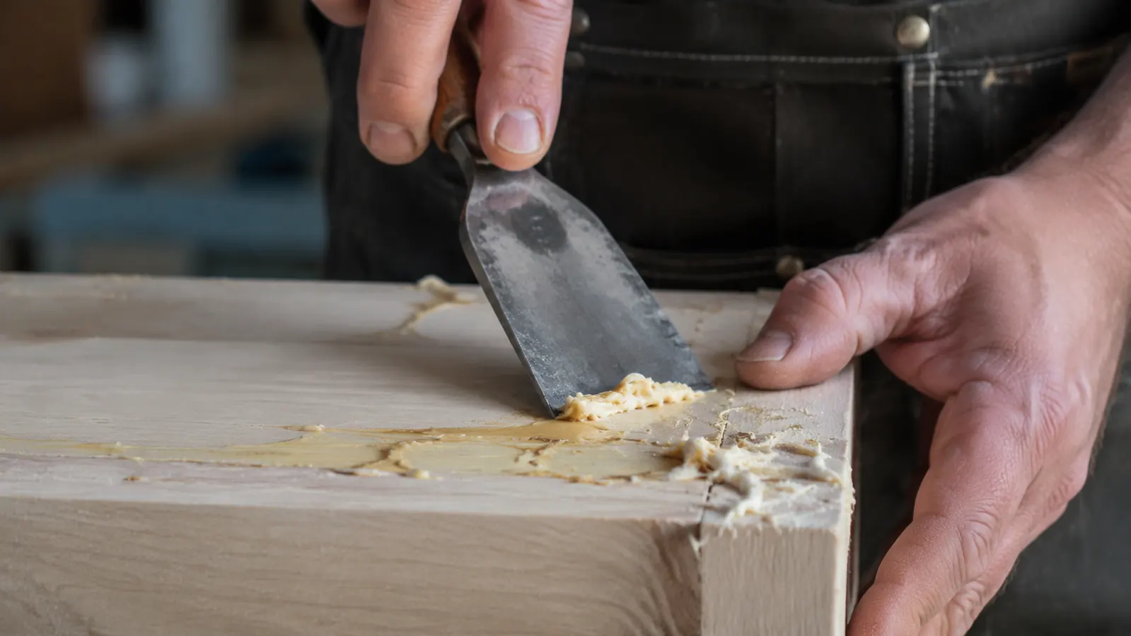 Close-up of glue squeeze-out on a panel joint being scraped with a chisel at a low angle