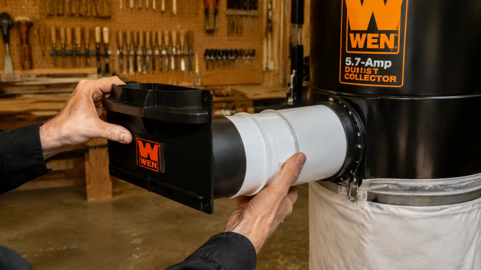 Hand installing a blast gate on a 4-inch PVC duct branch in a woodshop