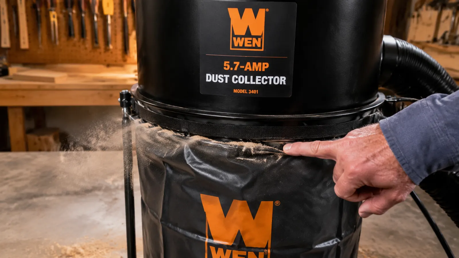 Close-up of a dust collector collection bag showing a fine dust haze around the seam, with a hand gesturing toward it