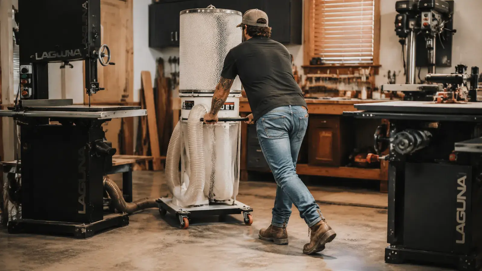 Woodworker rolling the WEN dust collector on its mobile base between a table saw and a bandsaw